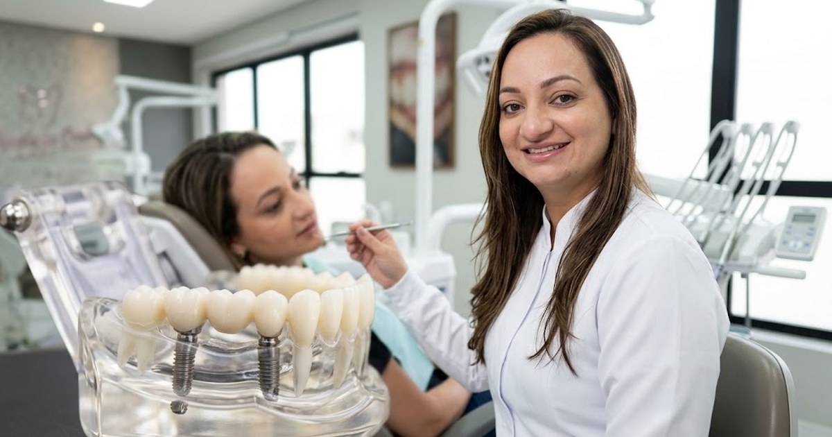 Ponte fixa sobre implante: Dra. Andréia Castro mostrando a paciente um modelo de ponte de três dentes apoiada em dois implantes no consultório em São Caetano do Sul